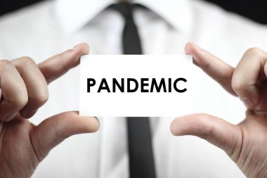 Beyaz gömlekli bir işadamı elinde PANDEMIC yazan bir kartvizit tutuyor. Coronavirus (COVID-19) küresel hastalık 2020.