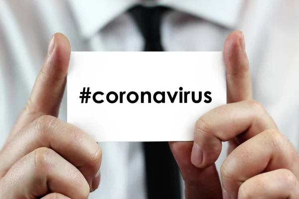 Beyaz gömlekli bir işadamı elinde CORONAVIRUS (hashtag 'li, sosyal medyada popüler) yazan bir kartvizit tutuyor. Coronavirus (COVID-19) küresel hastalık 2020.