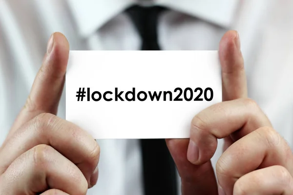ホワイトのシャツを着たビジネスマンが Lockdown 2020 ハッシュタグ付き ソーシャルメディアで人気 という言葉で名刺を手にしている コロナウイルス Covid Global Disease — ストック写真