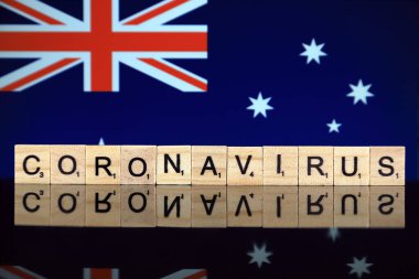 WROCLAW, POLAND - 28 Mart 2020: Kelime CORONAVIRUS ahşap harflerden yapılmış, ve arka planda Avustralya Bayrağı. Coronavirus (COVID-19) küresel hastalık 2020.