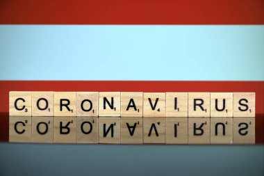 WROCLAW, POLAND - 28 Mart 2020: Kelime CORONAVIRUS ahşap harflerden yapılmış, ve arka planda Avusturya Bayrağı. Coronavirus (COVID-19) küresel hastalık 2020.