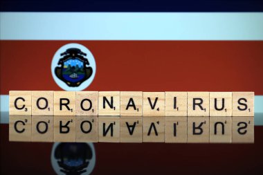 WROCLAW, POLAND - 28 Mart 2020: Kelime CORONAVIRUS ahşap harflerden yapılmış, ve arkasında Kosta Rika Bayrağı. Coronavirus (COVID-19) küresel hastalık 2020.