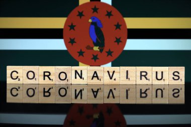WROCLAW, POLAND - 28 Mart 2020: Kelime CORONAVIRUS ahşap harflerden yapılmış, ve arka planda Dominica Flag. Coronavirus (COVID-19) küresel hastalık 2020.