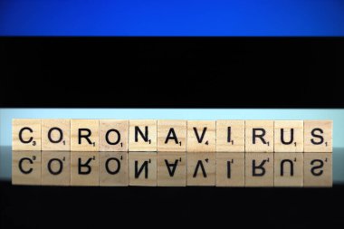 WROCLAW, POLAND - 28 Mart 2020: Kelime CORONAVIRUS ahşap harflerden yapılmış, ve arka planda Estonya Bayrağı. Coronavirus (COVID-19) küresel hastalık 2020.