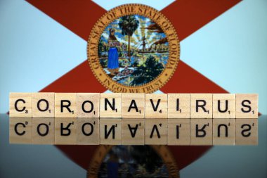 WROCLAW, POLAND - 28 Mart 2020: söz CORONAVIRUS ahşap harflerden yapılmış, ve Florida State Flag arka planda. Coronavirus (COVID-19) küresel hastalık 2020.