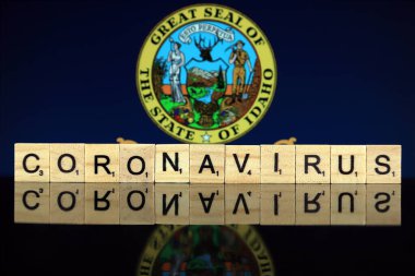 WROCLAW, POLAND - 28 Mart 2020: söz CORONAVIRUS ahşap harflerden yapılmış, ve arka planda Idaho State Flag. Coronavirus (COVID-19) küresel hastalık 2020.
