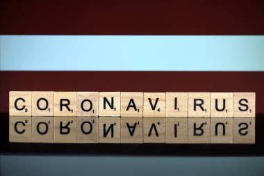 WROCLAW, POLAND - 28 Mart 2020: söz CORONAVIRUS ahşap harflerden yapılmış, ve arka planda Letonya Bayrağı. Coronavirus (COVID-19) küresel hastalık 2020.