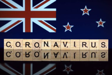 WROCLAW, POLAND - 28 Mart 2020: Kelime CORONAVIRUS ahşap harflerden yapılmış, ve arka planda Yeni Zelanda Bayrağı. Coronavirus (COVID-19) küresel hastalık 2020.