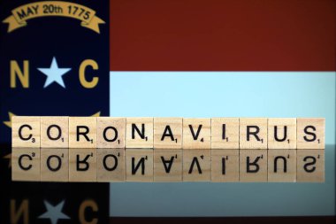 WROCLAW, POLAND - 28 Mart 2020: söz CORONAVIRUS ahşap harflerden yapılmış, ve arka planda Kuzey Carolina Bayrağı. Coronavirus (COVID-19) küresel hastalık 2020.