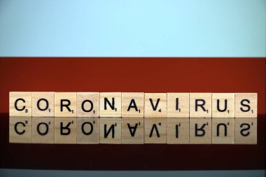 WROCLAW, POLAND - 28 Mart 2020: Kelime CORONAVIRUS ahşap harflerden yapılmış, ve arka planda Polonya Bayrağı. Coronavirus (COVID-19) küresel hastalık 2020.