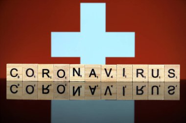 WROCLAW, POLAND - 28 Mart 2020: Kelime CORONAVIRUS ahşap harflerden yapılmış, ve arka planda İsviçre Bayrağı. Coronavirus (COVID-19) küresel hastalık 2020.