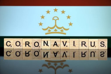 WROCLAW, POLAND - 28 Mart 2020: Kelime CORONAVIRUS ahşap harflerden yapılmış, ve arka planda Tacikistan Bayrağı. Coronavirus (COVID-19) küresel hastalık 2020.