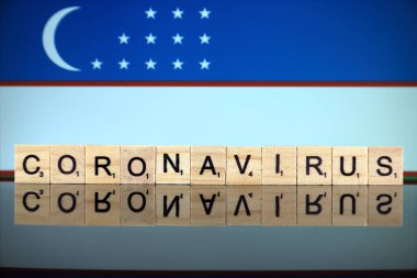 WROCLAW, POLAND - 28 Mart 2020: Kelime CORONAVIRUS ahşap harflerden yapılmış, ve arka planda Özbekistan Bayrağı. Coronavirus (COVID-19) küresel hastalık 2020.