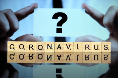 WROCLAW, POLAND - 30 Mart 2020 CORONAVIRUS sözcüğü ahşap harflerden yapılmış, ve arka planda soru işareti olan bir kartvizit tutan adam. Coronavirus (COVID-19) küresel hastalık 2020.