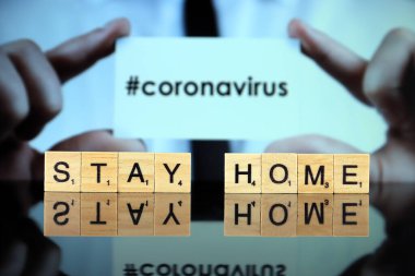 WROCLAW, POLAND - 30 Mart 2020: Ahşap harflerden yapılmış KONAVIRUS sözcüğü ve arka planda CORONAVIRUS (hashtag ile, sosyal medya popüler) sözcüğü ile bir kartvizit tutan adam.