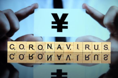 WROCLAW, POLAND - 30 Mart 2020: ahşap harflerden yapılmış CORONAVIRUS sözcüğü, ve arka planda yen veya yuan işareti olan bir kartvizit tutan adam. Coronavirus (COVID-19) küresel hastalık 2020.
