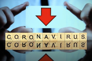 WROCLAW, POLAND - 30 Mart 2020 CORONAVIRUS sözcüğü ahşap harflerden yapılmıştır ve arka planda kırmızı ok olan bir kartvizit tutan adam. Coronavirus (COVID-19) küresel hastalık 2020.