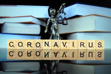 WROCLAW, POLAND - 30 Mart 2020: CORONAVIRUS kelimesi ahşap harflerden yapılmış, ve arka planda hukukun ve adaletin sembolü. Coronavirus (COVID-19) küresel hastalık 2020.