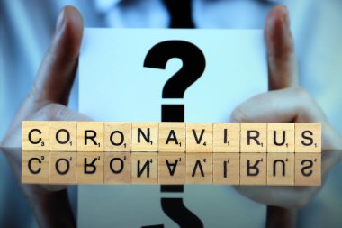 WROCLAW, POLAND - 30 Mart 2020 CORONAVIRUS sözcüğü ahşap harflerden yapılmış, ve arka planda soru işareti olan bir kartvizit tutan adam. Coronavirus (COVID-19) küresel hastalık 2020.