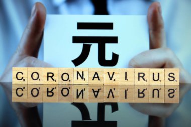 WROCLAW, POLAND - 30 Mart 2020: ahşap harflerden yapılmış CORONAVIRUS sözcüğü, ve arkasında Çince Yuan işareti olan bir kartvizit tutan adam. Coronavirus (COVID-19) küresel hastalık 2020.