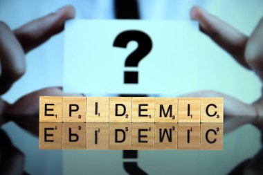 WROCLAW, POLAND - 30 Mart 2020: ahşap harflerden yapılmış EPIDEMIC kelimesi, ve arka planda soru işareti olan bir kartvizit tutan adam. Coronavirus (COVID-19) küresel hastalık 2020.