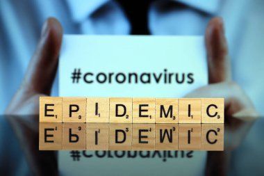 WROCLAW, POLAND - 30 Mart 2020: ahşap harflerden yapılmış EPIDEMIC sözcüğü, ve arka planda CORONAVIRUS sözcüğü olan bir kartvizit tutan adam. Coronavirus (COVID-19) küresel hastalık 2020.