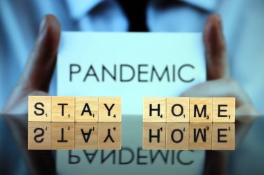 WROCLAW, POLAND - 30 Mart 2020: sözcükler ahşap harflerden yapılmış ev kalır, ve arka planda PANDEMIC kelimesi olan bir kartvizit tutan adam. Coronavirus (COVID-19) küresel hastalık 2020.
