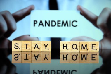 WROCLAW, POLAND - 30 Mart 2020: sözcükler ahşap harflerden yapılmış ev kalır, ve arka planda PANDEMIC kelimesi olan bir kartvizit tutan adam. Coronavirus (COVID-19) küresel hastalık 2020.