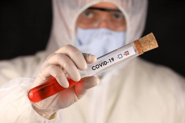 Koruyucu giysili ve maskeli doktor, hızla yayılan Coronavirus 'un pozitif kan testi sonucunu içeren cam bir tüp tutuyor. Küresel koronavirüs hastalığı (COVID-19) 2020.