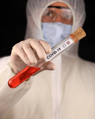 Koruyucu giysili ve maskeli doktor, hızla yayılan Coronavirus 'un pozitif kan testi sonucunu içeren cam bir tüp tutuyor. Küresel koronavirüs hastalığı (COVID-19) 2020.