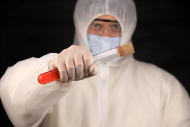 Koruyucu giysili ve maskeli doktor hızla yayılan Coronavirus için kan testi yapılan cam bir tüp tutuyor. Küresel koronavirüs hastalığı (COVID-19) 2020.
