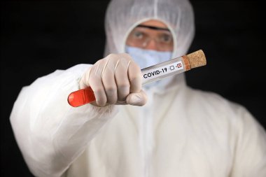 Koruyucu giysili ve maskeli doktor, hızla yayılan Coronavirus 'un pozitif kan testi sonucunu içeren cam bir tüp tutuyor. Küresel koronavirüs hastalığı (COVID-19) 2020.