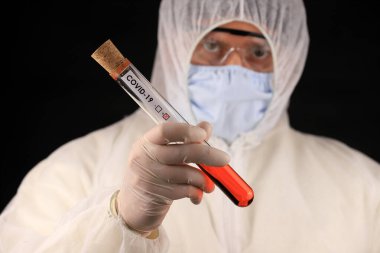 Koruyucu giysili ve maskeli doktor, hızla yayılan Coronavirus 'un pozitif kan testi sonucunu içeren cam bir tüp tutuyor. Küresel koronavirüs hastalığı (COVID-19) 2020.