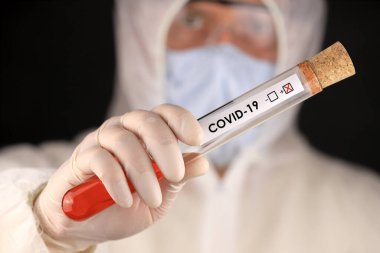 Koruyucu giysili ve maskeli doktor, hızla yayılan Coronavirus 'un pozitif kan testi sonucunu içeren cam bir tüp tutuyor. Küresel koronavirüs hastalığı (COVID-19) 2020.
