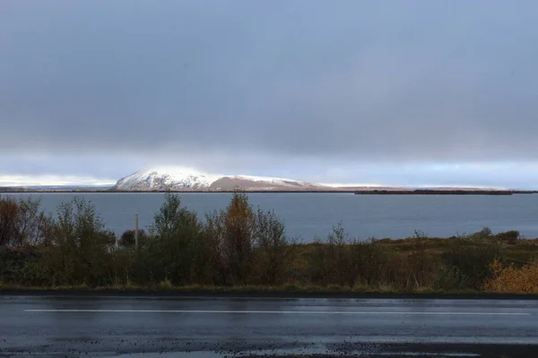 Camino frente a una pequeña montaña cubierta de nieve — Foto de Stock