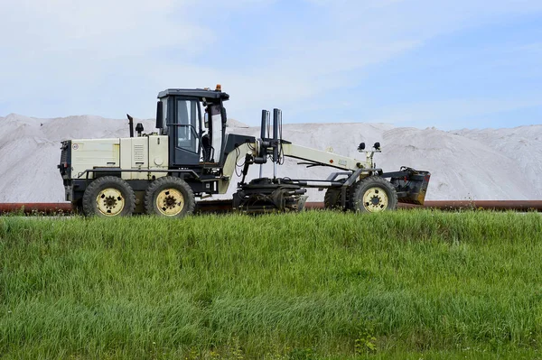 The grader is at the dam with pipeline in the background of mine. Side view. Foreground green grass — Stock Photo, Image