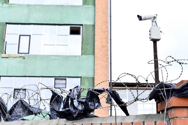 Videovigilancia de la cámara en el fondo del edificio montado en una pared de ladrillo, vallado con alambre de púas . — Foto de Stock