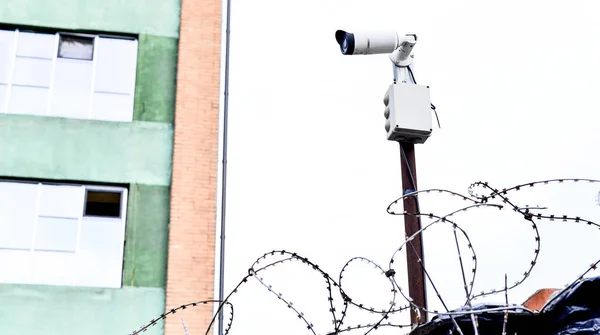 Videovigilancia de la cámara en el fondo del edificio montado en una pared de ladrillo, vallado con alambre de púas . — Foto de Stock
