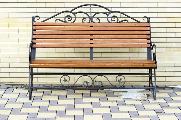 Brown Park bench against the wall of a light yellow brick. — Stock Photo, Image