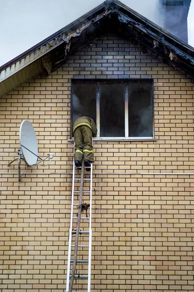 Um bombeiro apaga um edifício em chamas com escadas de extensão de altura — Fotografia de Stock