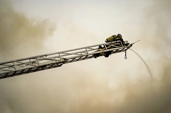 Un bombero apaga un edificio en llamas con escaleras de extensión de altura — Foto de Stock