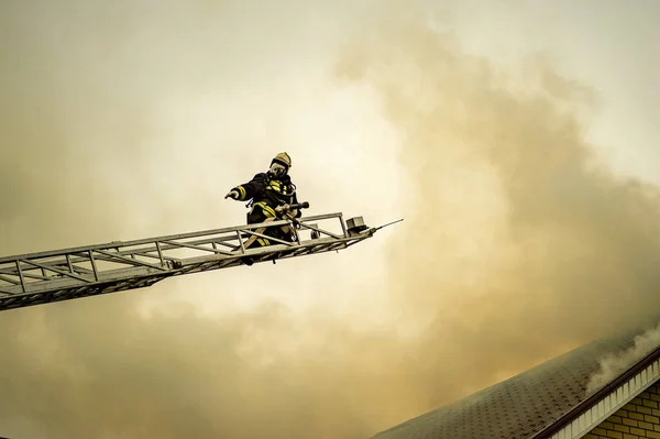 Seorang pemadam kebakaran memadamkan sebuah bangunan terbakar dengan tangga tambahan tinggi — Stok Foto