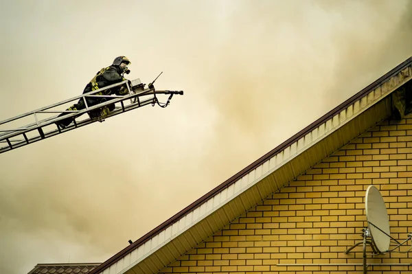 Um bombeiro apaga um edifício em chamas com escadas de extensão de altura — Fotografia de Stock