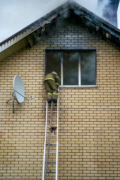 Un bombero apaga un edificio en llamas con escaleras de extensión de altura —  Fotos de Stock