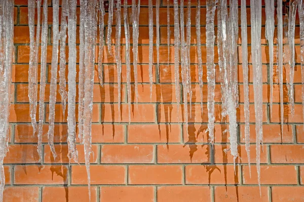 Na zdi z červených cihel budovy visí ledové rampouchy. Pozadí — Stock fotografie