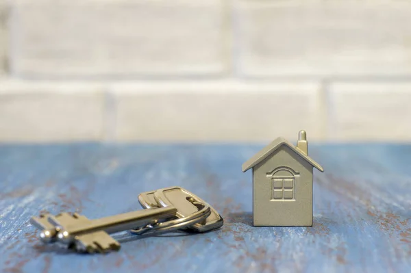 Símbolo de una casa con llaves de metal en una mesa vintage contra una pared blanca de ladrillo borroso . — Foto de Stock