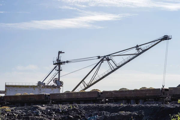 Uma enorme escavadora sobrecarrega na rocha de despejos do trem descarregado da mina contra um céu azul claro. Conceito: mineração e problemas ambientais — Fotografia de Stock