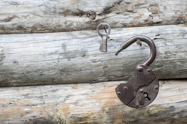 Una antigua cerradura de hierro forjado abierta y la llave cuelgan de los clavos contra una pared de madera. Contexto —  Fotos de Stock