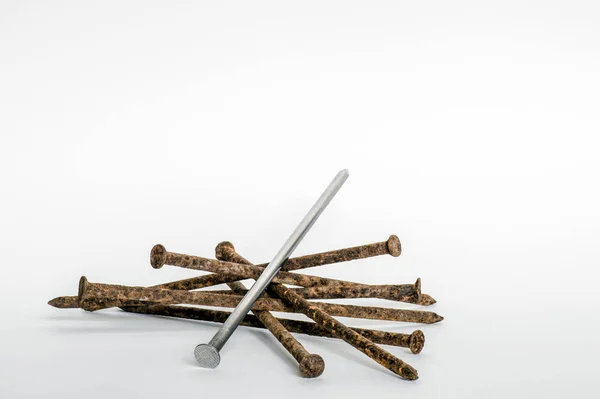 Metal new nail on a pile of old rusty nails on a white background. The concept of a new solution, look, uniqueness. — Stock Photo, Image