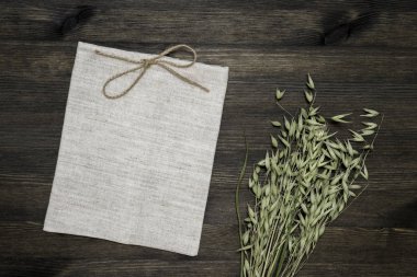 Küçük keten çanta jüt sicim ve koyu ahşap arka planda yeşil yulaf kulakları ile düğümlenmiş.